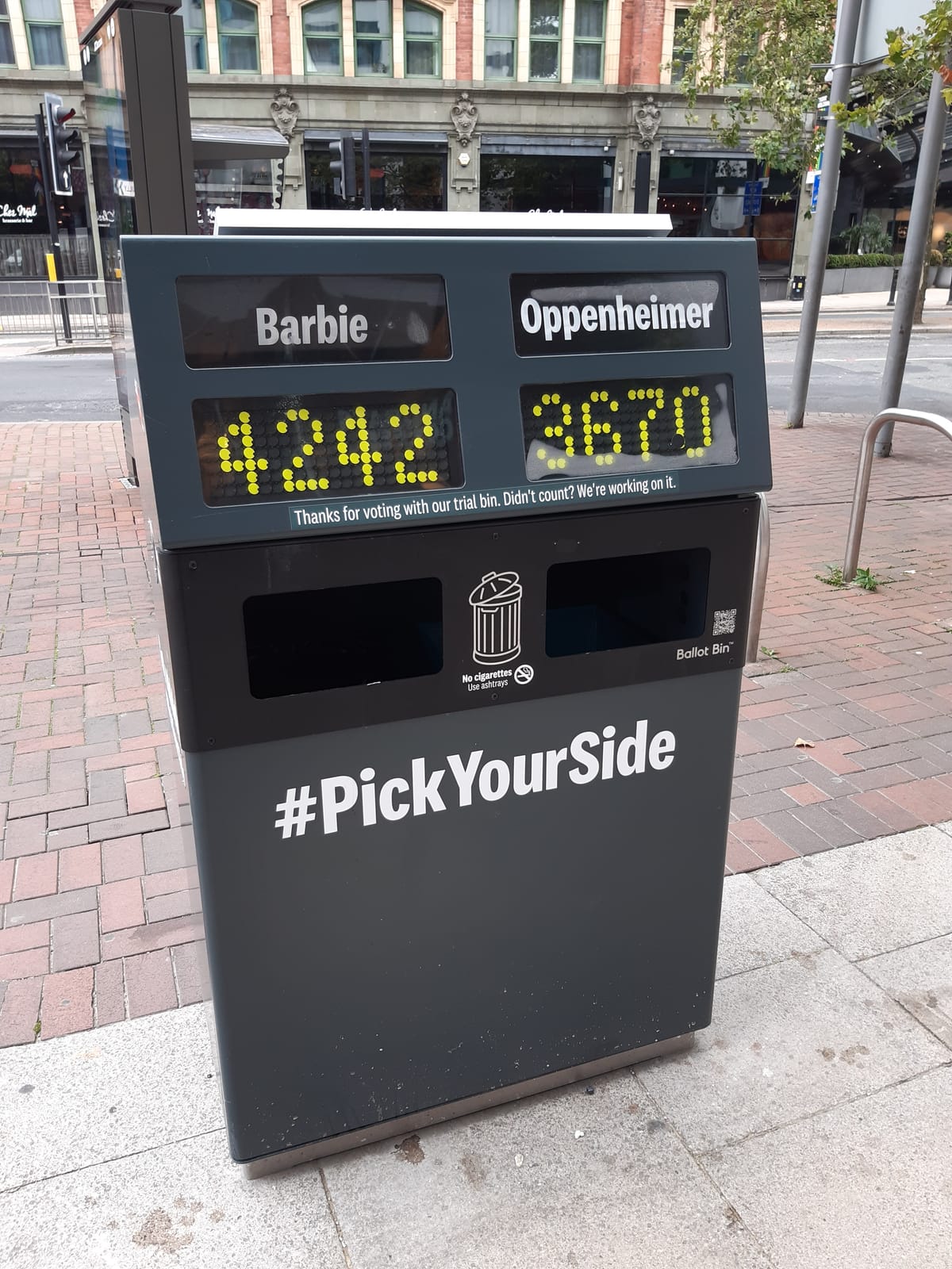 A trash can allowing people to "vote" with their litter for 'Barbie' or 'Oppenheimer.'