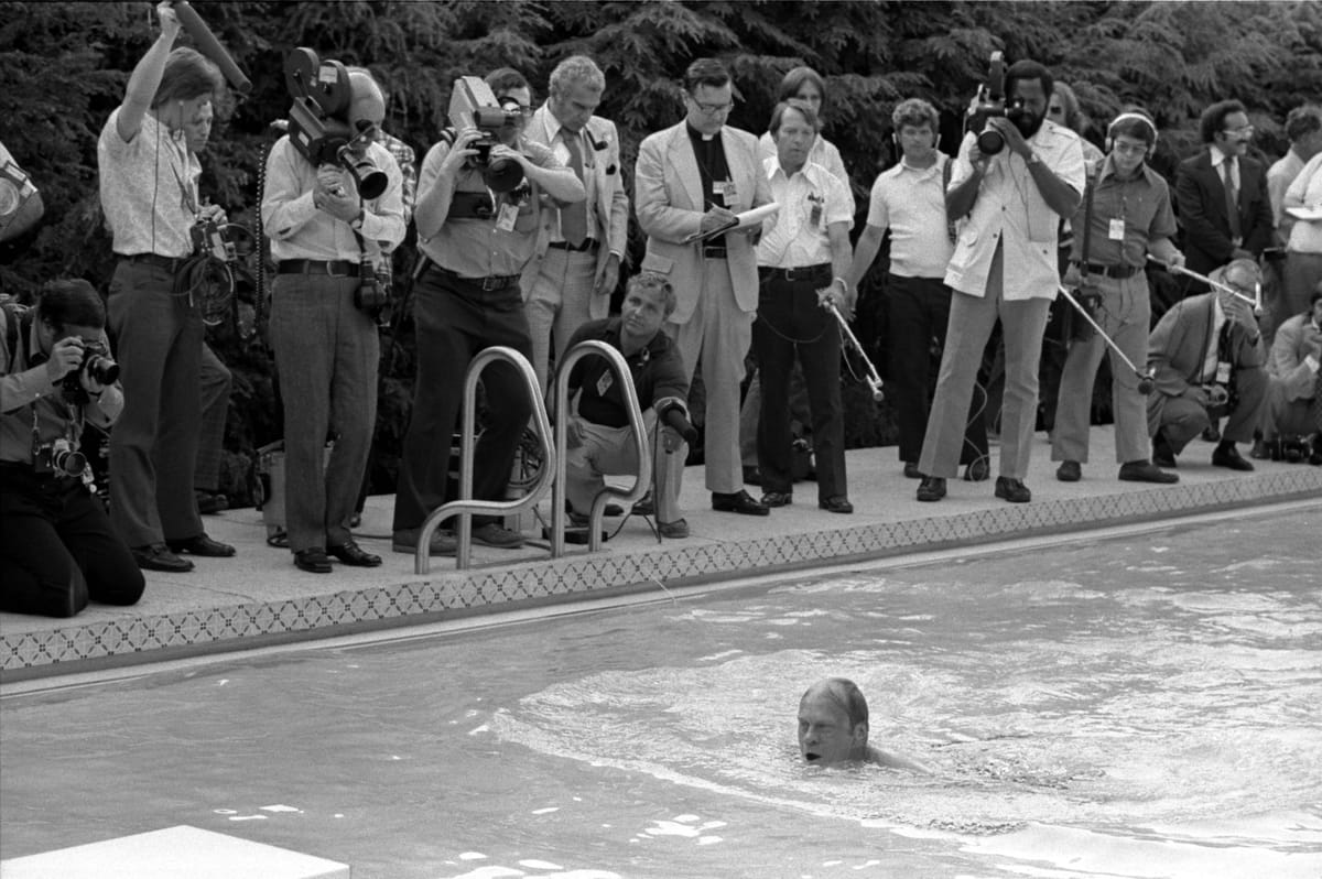 Black + white image of President Ford swimming in the White House pool as the press pool looks on. 